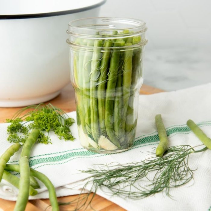 Ball Mason Jar filled with green beans sitting on a towel surrounded by green beans and dill sprigs 